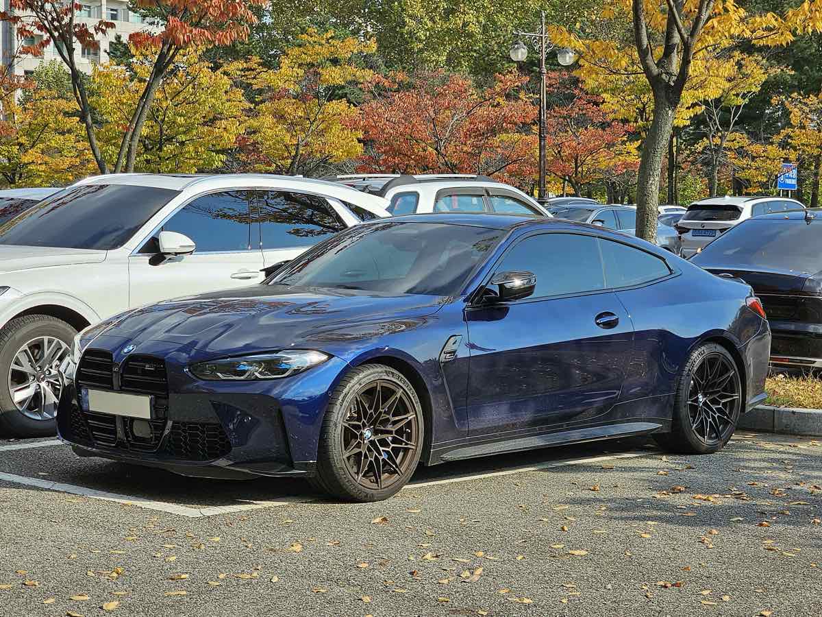 Side three-quarter view of a Tanzanite Blue 2022 BMW M4 Competition coupe